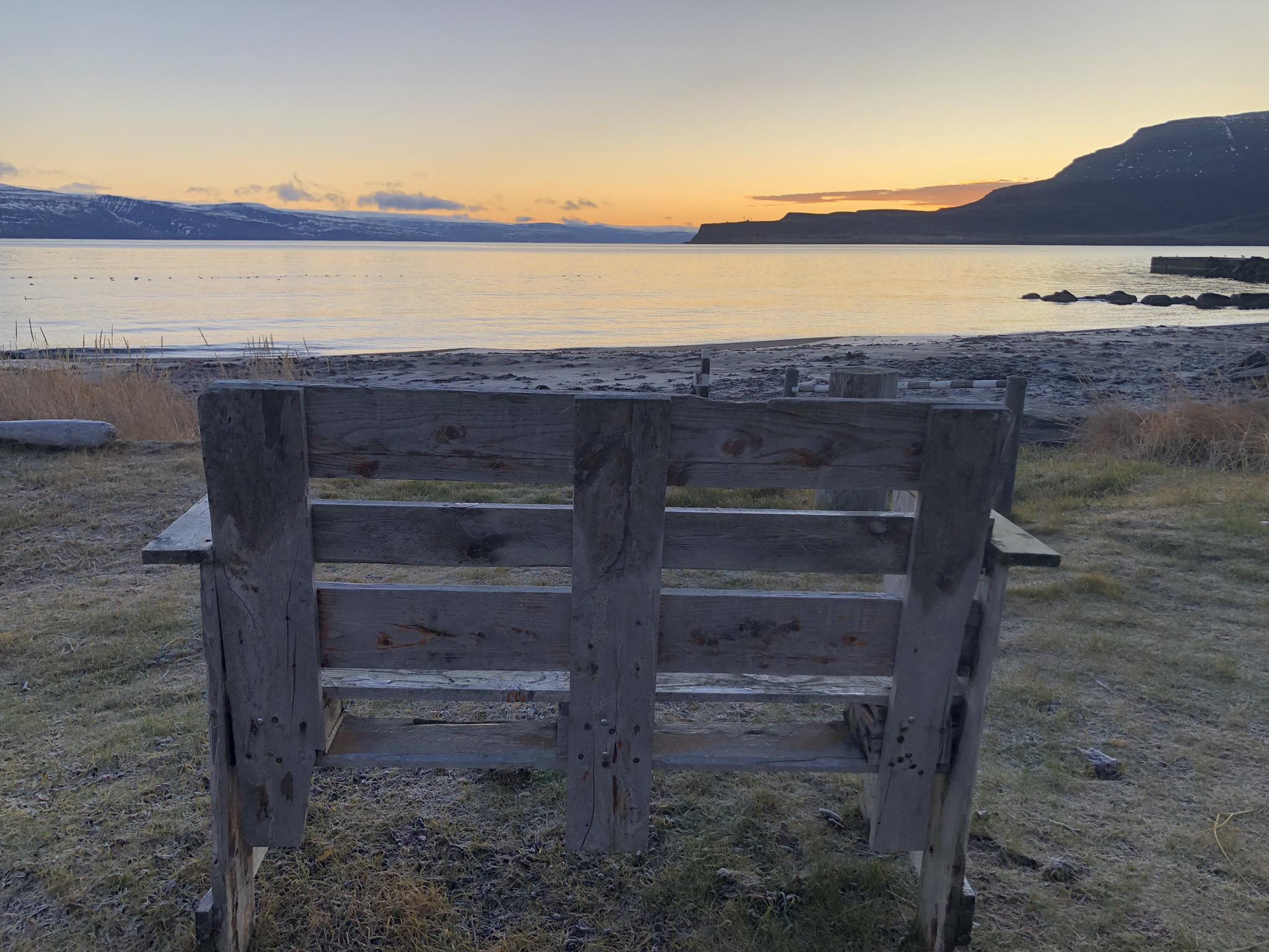 Fjaran Skeljavík í Hnífsdal að kvöldlagi. Bekkur í forgrunni og sólin sest.