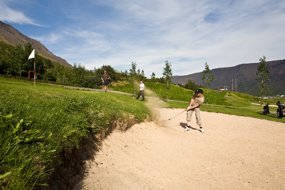 Maður að slá golfkúlu upp úr sandgryfju á golfvellinum í Tungudal.